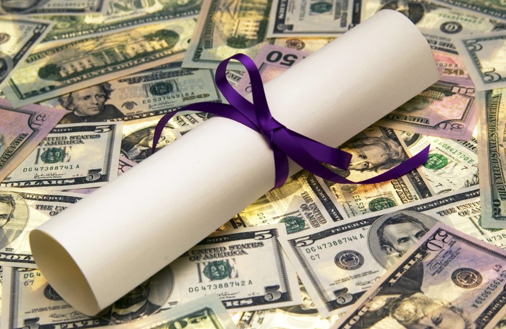 pile of money with rolled up diploma tied with a blue ribbon